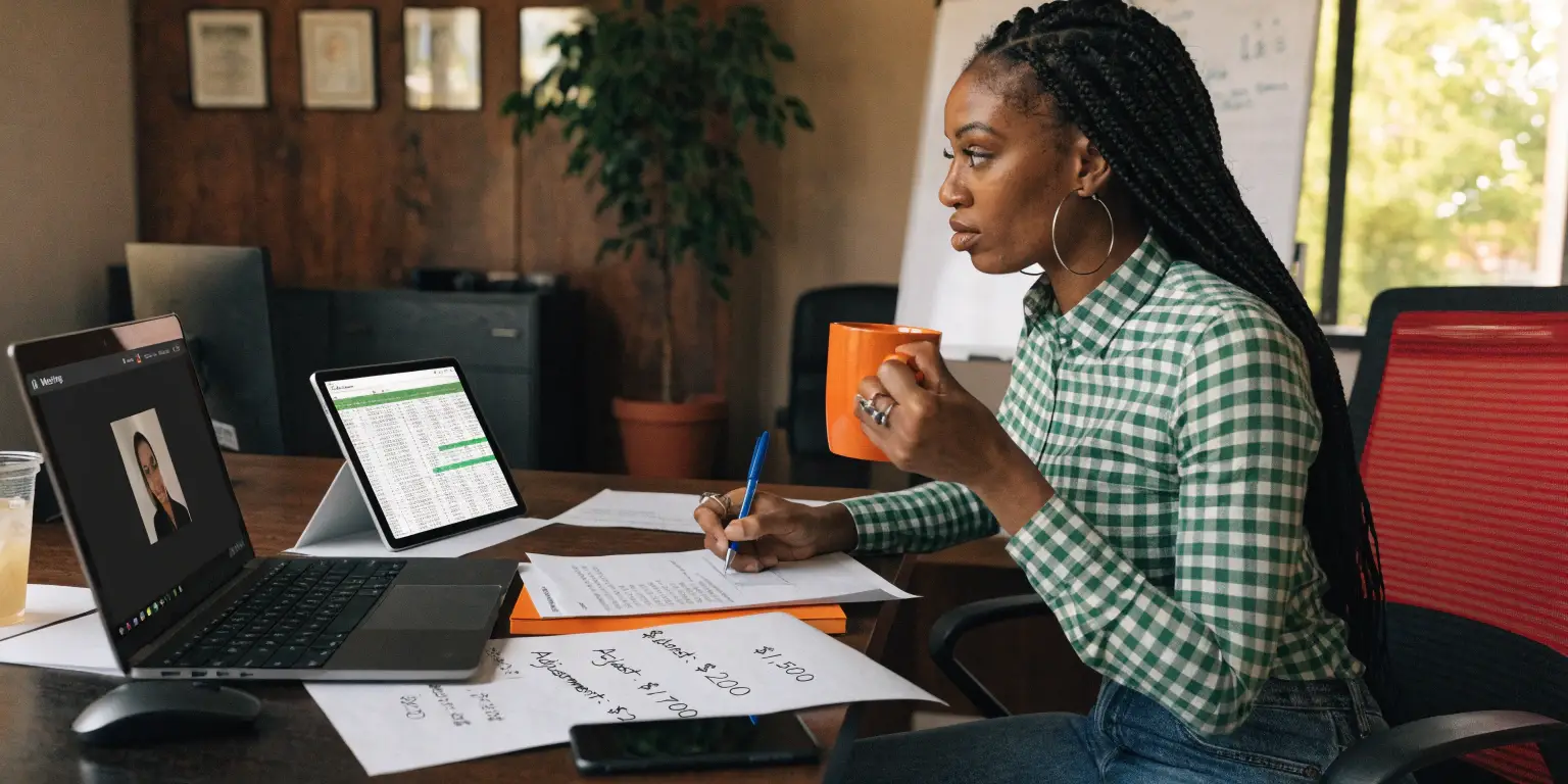 Woman in office participating in video call while reviewing documents and screens