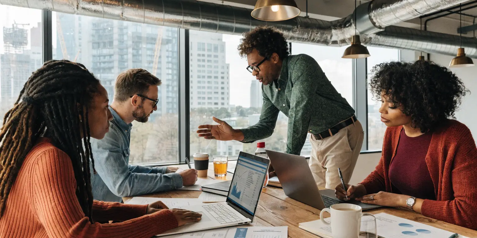 Diverse office team collaborating around table with laptops and charts